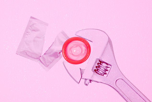 a red condom on a pink background is rotated by a wrench