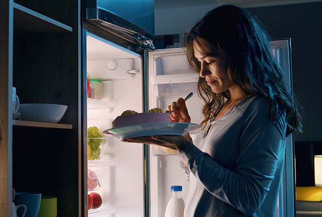 A woman eats food from a fridge during the early stages of her pregnancy.