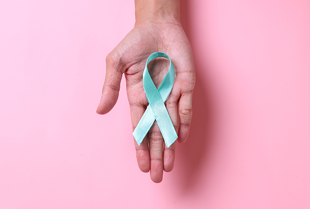 A light blue cancer ribbon lays in an open palm.