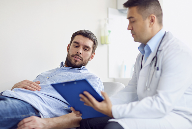 a man in a doctors office talks to a doctor in a white coat holding a clipboard