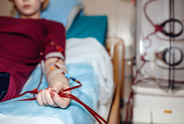 A woman lays on a hospital bed receiving dialysis. 