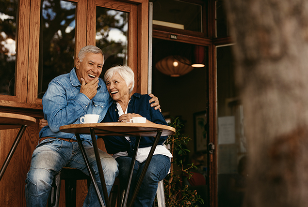 An older couple cuddle at a table outside of a restaurant on a date.