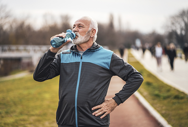 an older man in a track jacket sips from a blue water bottle