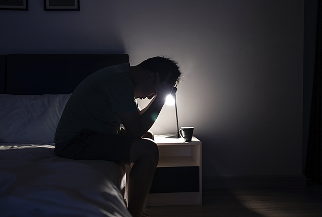 A man sits on the end of his bed with head in hands.