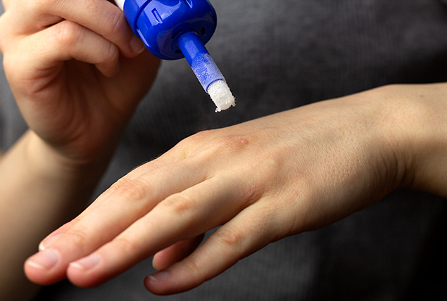 A hand holds ointment in their hand as they are able to apply it to a wart on the other hand.