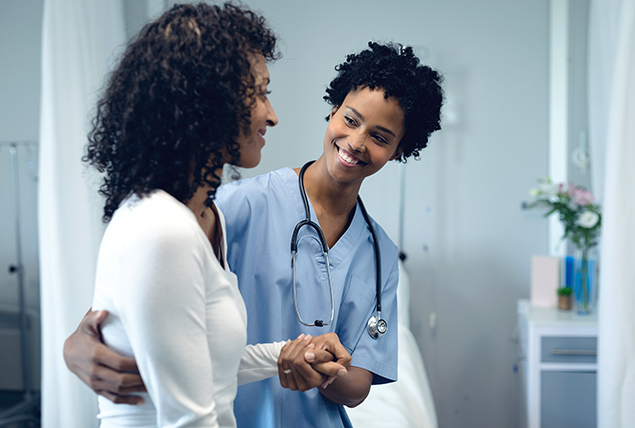 A black doctor smiles and holds her arm around a black woman.