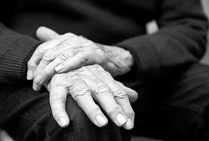 The hands of a senior man lay on his knee.