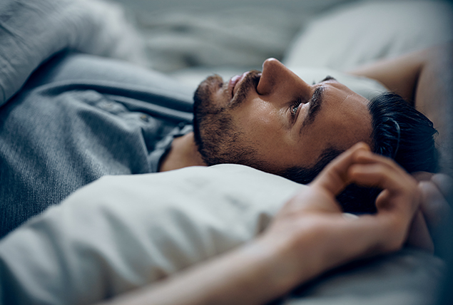 A man lays in bed with his arms over his head.