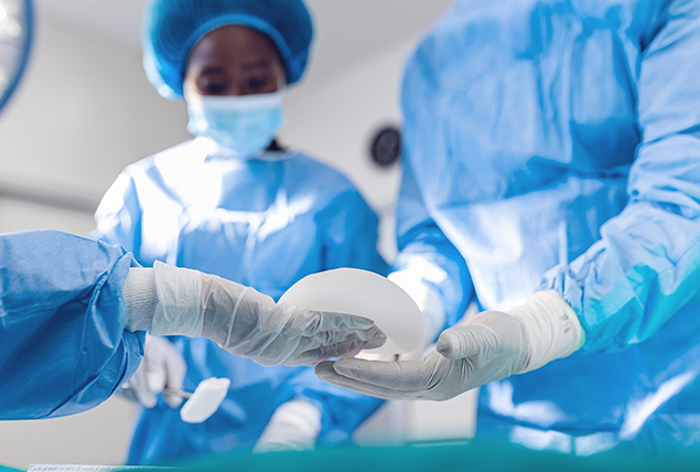 A surgical assistant hands a breast implant over to a surgeon. 
