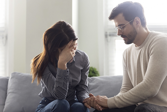 man comforts woman as she hides her face in sadness