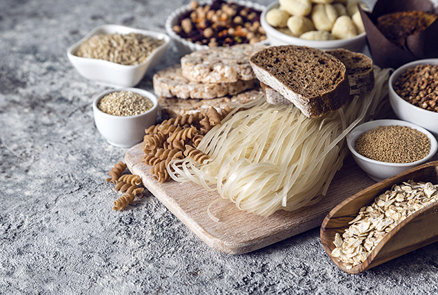 various pastas and grain are piled on a wooden cutting board