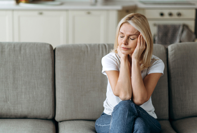 women sits on couch and holds her head in stress