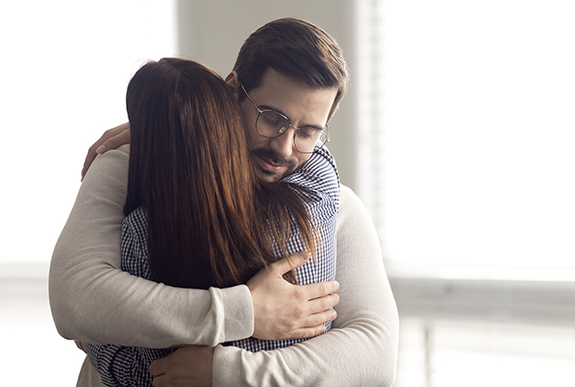 man with glasses hugs woman in brightly lit room
