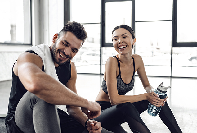 man and woman smile at each other in workout clothes in a gym 