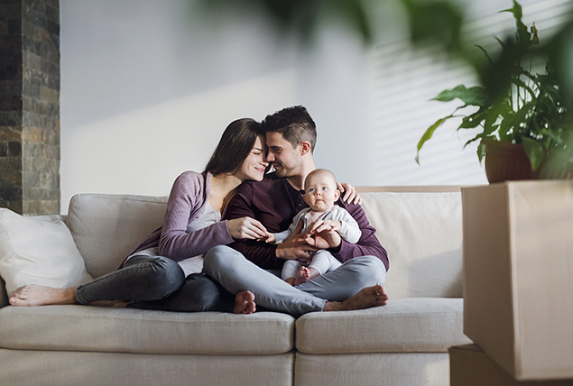a man and woman embrace on a tan couch with their baby