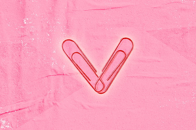two red paperclips form a heart on a pink papery background