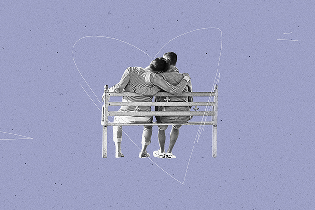 Two men sit hugging on a park bench with a thing white heart drawn around them.