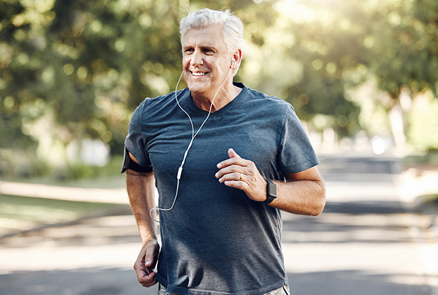 a man with gray hair smiles as he jogs outside while wearing headphones