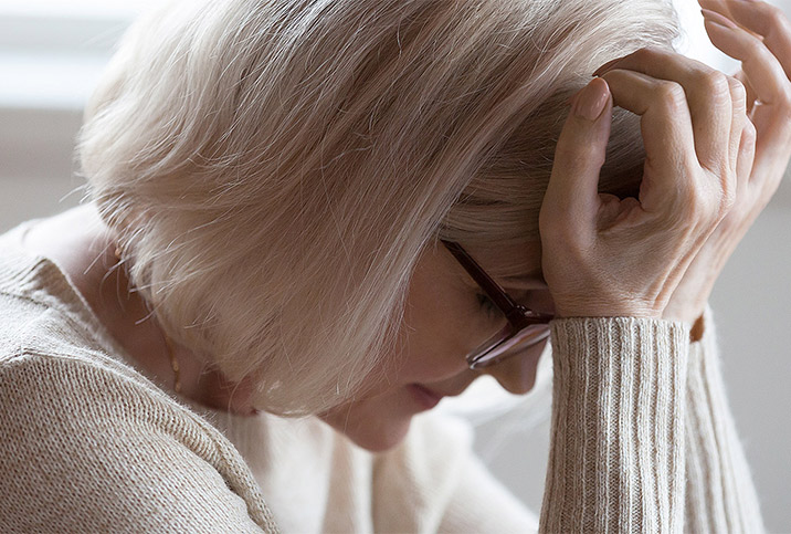 an older woman in a cream sweater places her head in her hands