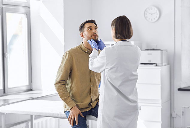 doctor in blue gloves looks at the face of a man in a brown shirt 