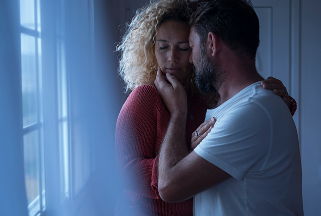 a man and a woman stand at a window as he kisses her cheek