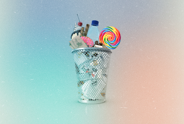 ice cream, candy, soda and other sugary foods in wire trashcan on marbled pastel background
