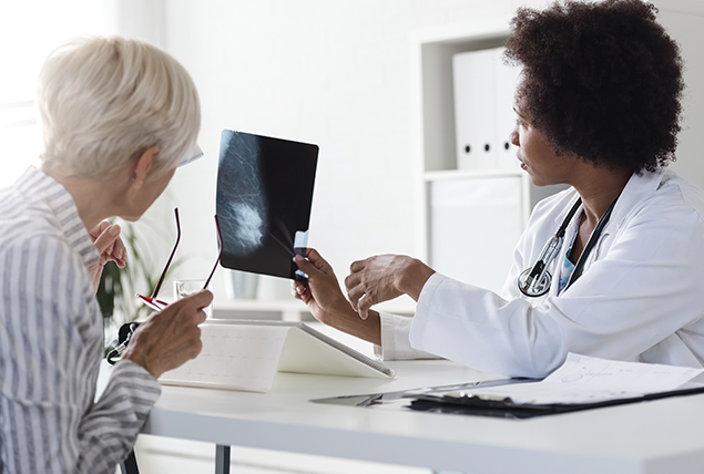 A doctor shows an x-ray of a breast to a patient sitting across the table.