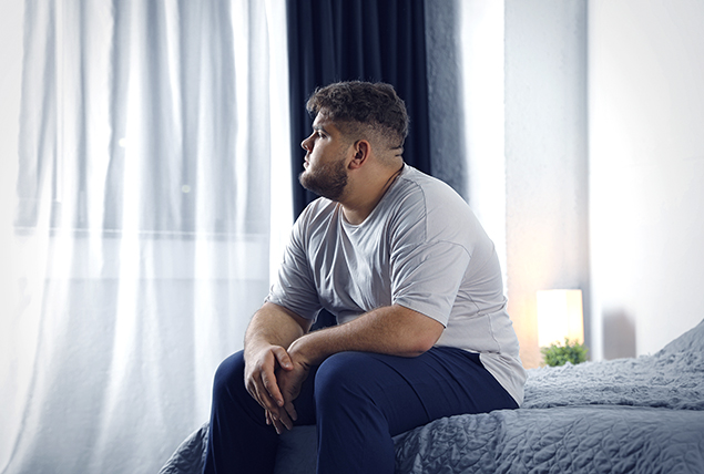 man in gray shirt looks concerned and sits on dark gray bed