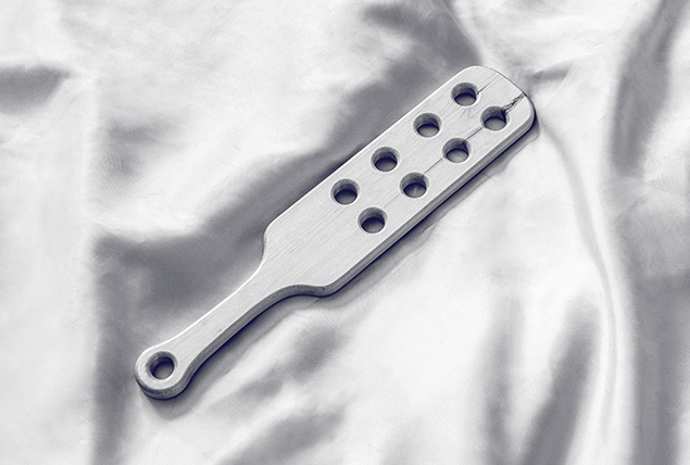 silver wooden paddle with holes on silver satin sheets