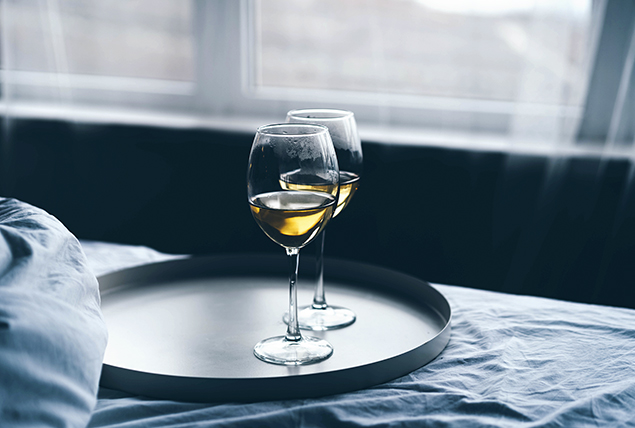 two glasses of white wine sit on a tray on a bed