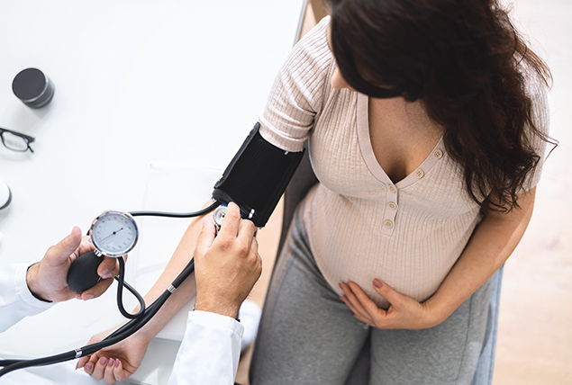 pregnant woman holds her belly and gets her blood pressure taken by doctor