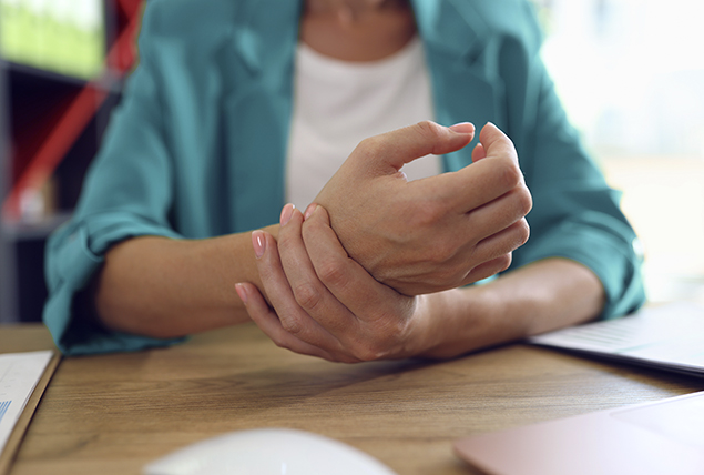 woman sits at table and holds her wrist in pain