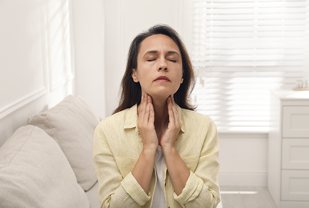 woman touches her throat with both hands and looks concerned