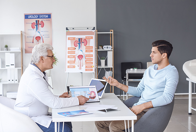 man sits and talks at table with doctor in white coat with testicular diagrams behind