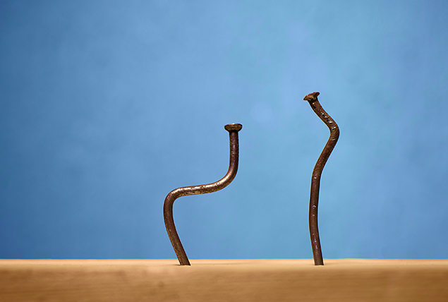 Two nails are bent while stuck in a wooden board against a blue background.