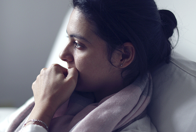 woman in gray cardigan chews her thumbnail looks anxious