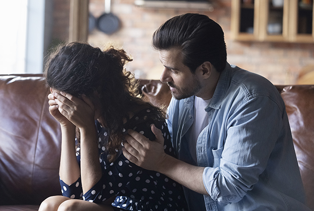 woman hides her face in her hands in stress as man touches her shoulder trying to comfort her