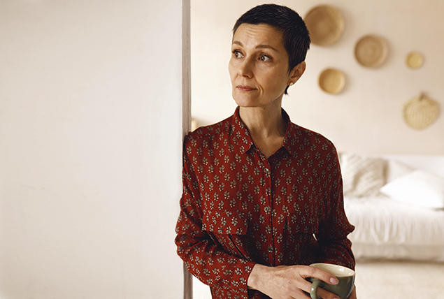 older woman with short haircut leans against doorframe and looks into the distance stressed