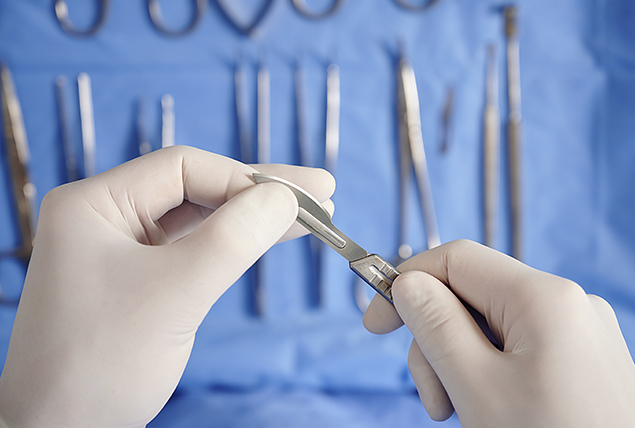 white gloved hairs hold scalpel with other surgical tools in the background 