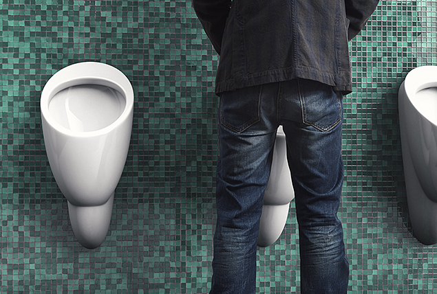 person wearing jeans standing in front of a urinal with green tiles 