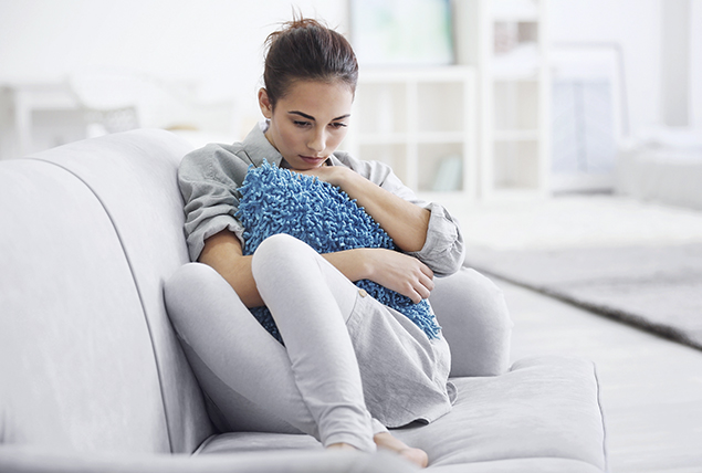 A woman sits on a sofa holding a pillow to her chest.