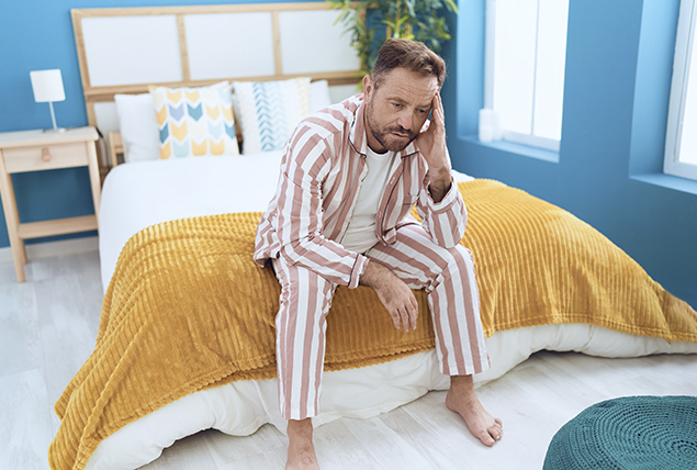 older man in striped pajamas looks worried and sits on bed with yellow blanket