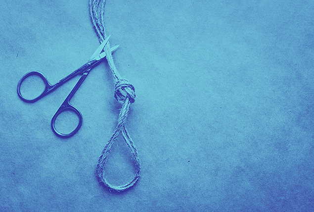 A pair of scissors are cutting part of a rope that is looped in the shape of a testicle.