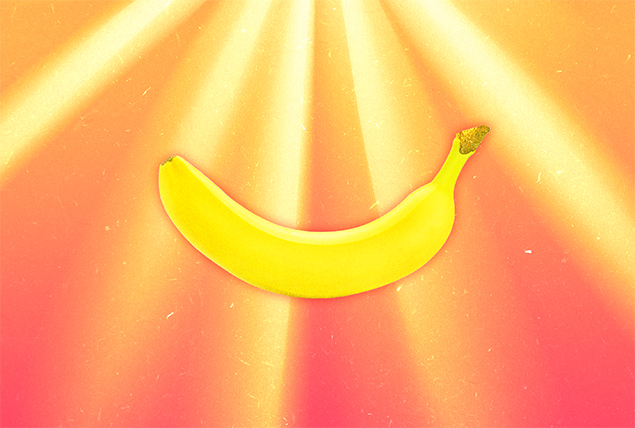 A banana is against an orange background with yellow beams of sunlight shining down on it.