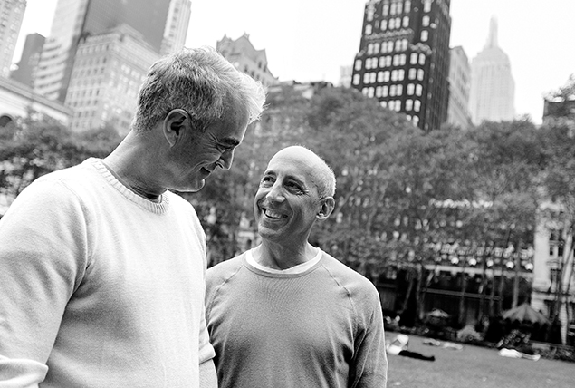 Two men embrace while smiling at each other in a park.