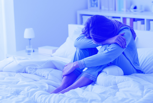 woman with blue tint sits on bed with head on knees in depression