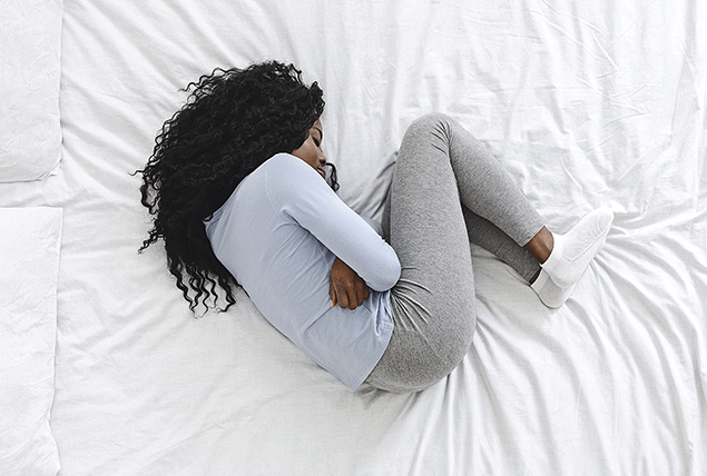 woman curled up in fetal position on white bed in pain 