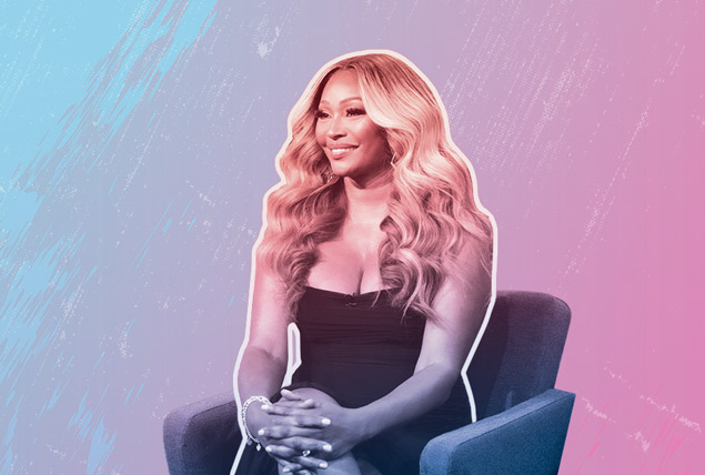 Cynthia Bailey sits on a chair looking away and smiling.