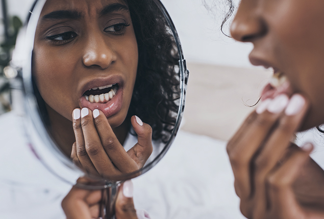 woman checks her teeth and gums in magnifying mirror and looks concerned