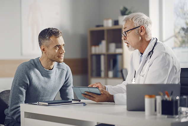 doctor in white coat talks with older male patient and gestures to tablet